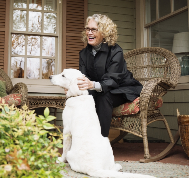 Woman smiling in jacket outside petting cream colored dog.